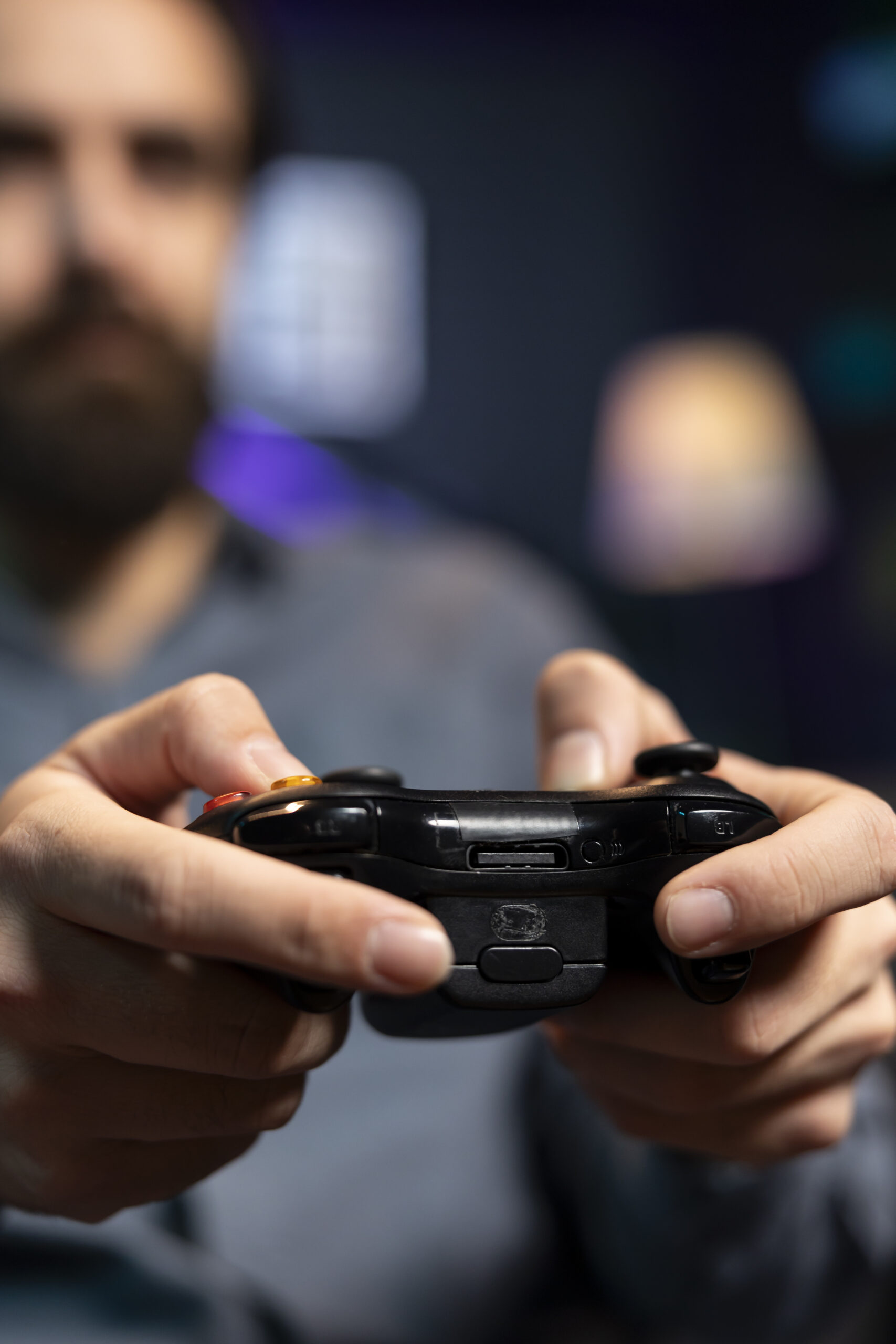 Focus shot on controller held by man defeating enemies while playing videogames on gaming console with teammates. Player in blurry background using gamepad to participate in esports game